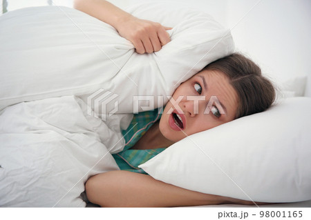 Emotional young woman covering ears with pillows at home in morning 98001165