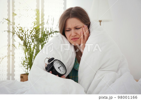 Sleepy young woman with alarm clock at home in morning 98001166