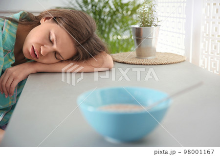 Young woman sleeping at table in morning 98001167