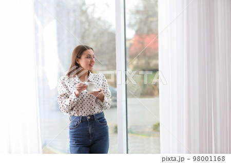Young woman with cup near window indoors 98001168