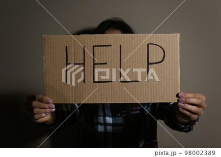 Young woman with sign HELP near beige wall. Domestic violence concept 98002389