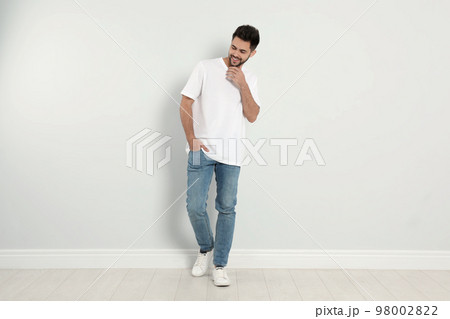 Young man in stylish jeans near light wall 98002822