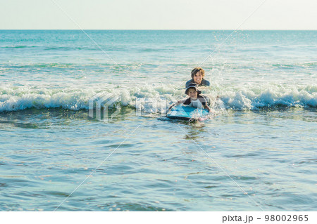 Father teaching his young son how to surf in the sea on vacation or holiday. Travel and sports with children concept 98002965