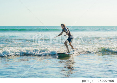 Young man, beginner Surfer learns to surf on a sea foam on the Bali island Young man, beginner Surfer learns to surf on a sea foam on the Bali island 98002966