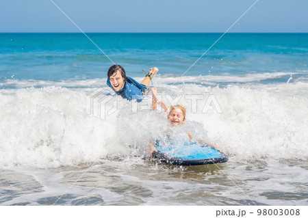 Father teaching his young son how to surf in the sea on vacation or holiday. Travel and sports with children concept Father teaching his young son how to surf in the sea on vacation or holiday. Travel and sports with children concept 98003008