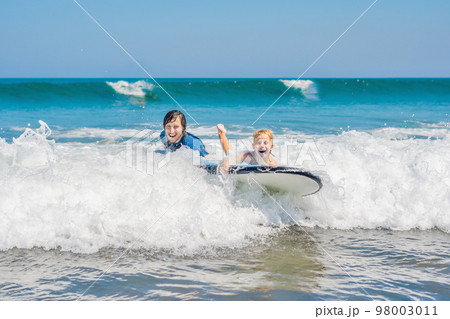 Father teaching his young son how to surf in the sea on vacation or holiday. Travel and sports with children concept Father teaching his young son how to surf in the sea on vacation or holiday. Travel and sports with children concept 98003011