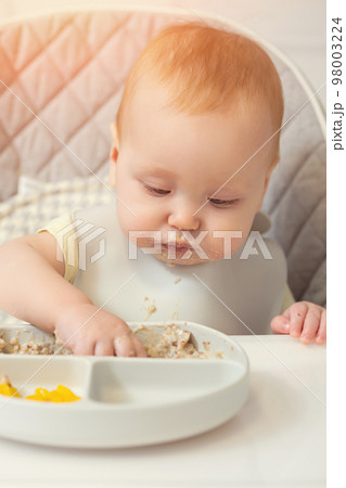 Excited baby girl touches food leftovers on plate and tastes 98003224