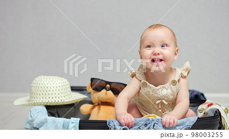 Happy baby girl sitting in suitcase smiles and laughs 98003255