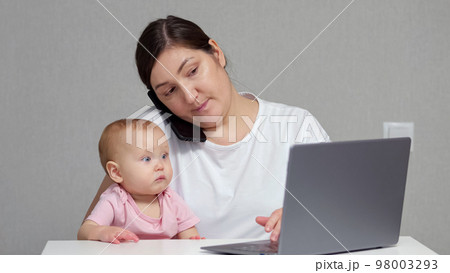 Brunette mother talks with colleague on phone holding baby 98003293
