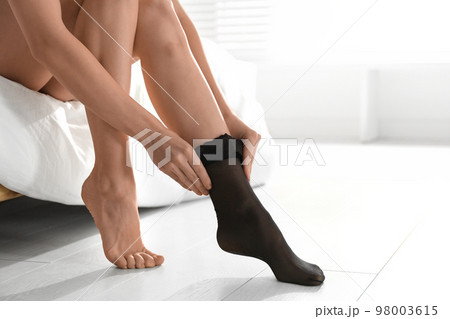 Young woman putting on stocking in bedroom, closeup 98003615