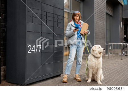 Woman receiving a parcel from automatic post machine during a walk with her dog Woman receiving a parcel from automatic post machine during a walk with her dog 98003684