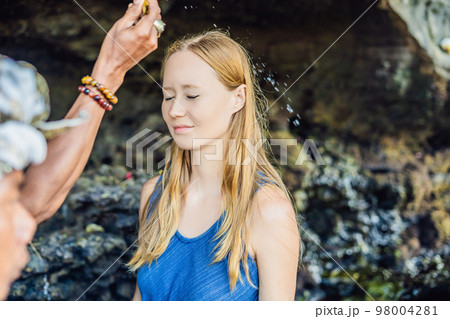 Woman is a tourist in Bali. The ritual of ablution with holy water and on her forehead prikleeli rice and put the flower ear Woman is a tourist in Bali. The ritual of ablution with holy water and on her forehead prikleeli rice and put the flower ear 98004281