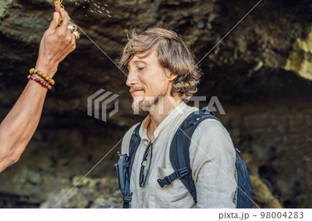 Man is a tourist in Bali. The ritual of ablution with holy water and on her forehead prikleeli rice and put the flower ear Man is a tourist in Bali. The ritual of ablution with holy water and on her forehead prikleeli rice and put the flower ear 98004283