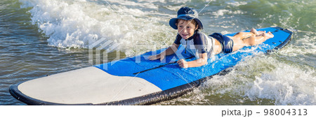 Happy baby boy - young surfer ride on surfboard with fun on sea waves. Active family lifestyle, kids outdoor water sport lessons and swimming activity in surf camp. Summer vacation with child BANNER 98004313