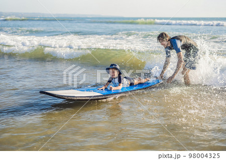 Father teaching his young son how to surf in the sea on vacation or holiday. Travel and sports with children concept Father teaching his young son how to surf in the sea on vacation or holiday. Travel and sports with children concept 98004325