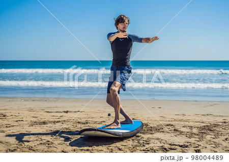 Young man surfer training before go to lineup on a sand beach. Learning to surf. Vacation concept. Summer holidays. Tourism, sport Young man surfer training before go to lineup on a sand beach. Learning to surf. Vacation concept. Summer holidays. Tourism, sport 98004489