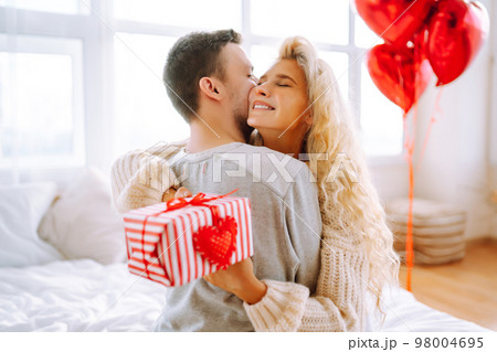 Beautiful young couple at home celebrating Valentine's Day. Lovers give each other gifts. 98004695