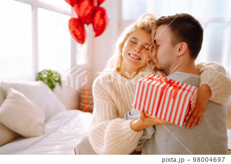 Beautiful young couple at home celebrating Valentine's Day. Lovers give each other gifts. 98004697
