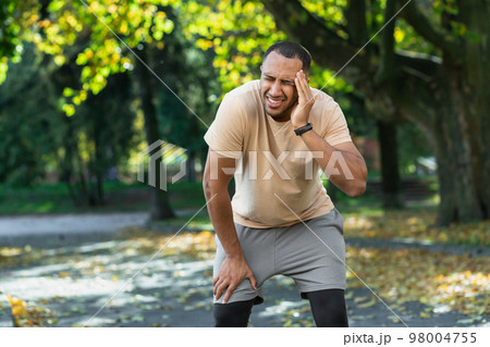 Man after jogging and fitness in the park has a bad headache, hispanic athlete on a run sick and tired. Man after jogging and fitness in the park has a bad headache, hispanic athlete on a run sick and tired. 98004755