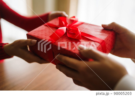 Valentine's Day, holiday and surprise concept. Man gives to his woman a red gift box. Valentine's Day, holiday and surprise concept. Man gives to his woman a red gift box. 98005203