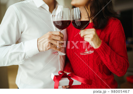 Couple clink glasses with red wine. Lovers give each other gifts. Lovely romantic dinner. Couple clink glasses with red wine. Lovers give each other gifts. Lovely romantic dinner. 98005467