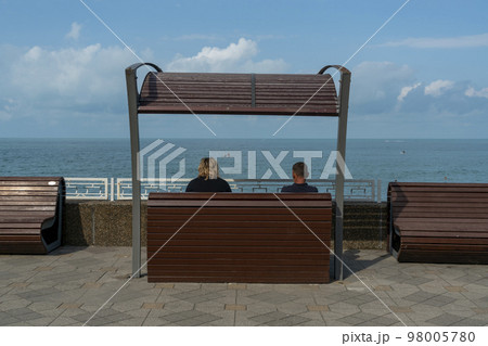 A man and a woman are sitting on a bench in front of the sea. 98005780