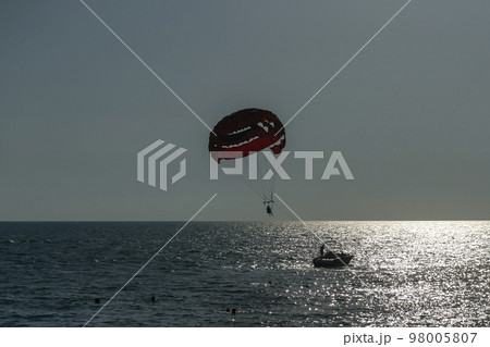 A man soars on a parachute over the sea behind a boat. 98005807