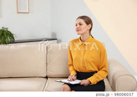 Professional psychotherapist with clipboard on sofa in office Professional psychotherapist with clipboard on sofa in office 98006037