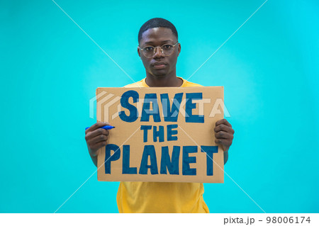 Young black man holding save the planet sign protesting climate change isolated on blue background. Young black man holding save the planet sign protesting climate change isolated on blue background. 98006174
