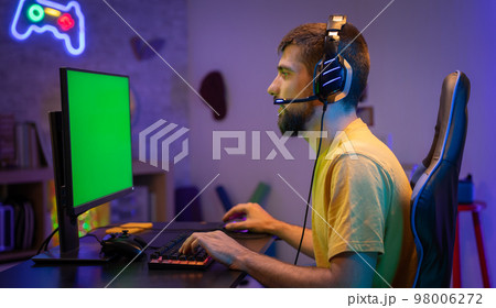 Pro gamer streaming video games with green screen mock-up display in gaming home studio. Chroma key. 98006272