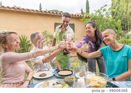 Happy friends toasting with big smile around the table at house patio diner. 98006366