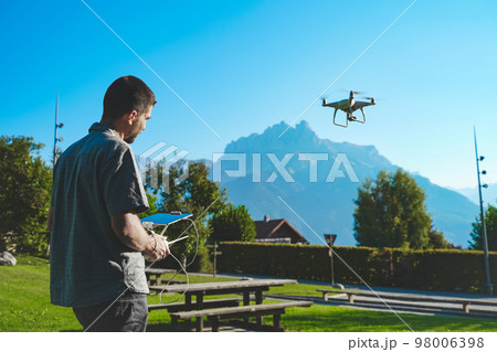 Young man flying drone on amazing mountain landscape. Man operating a drone with remote control taking aerial photos and videos. 98006398