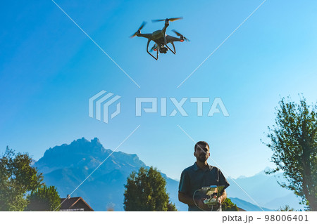 Young man flying drone on amazing mountain landscape. Man operating a drone with remote control taking aerial photos and videos. 98006401