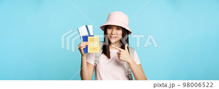 Smiling korean tourist shows her passport, vaccination certificate from coronavirus disease, getting vaccine shot to travel, standing over blue background Smiling korean tourist shows her passport, vaccination certificate from coronavirus disease, getting vaccine shot to travel, standing over blue background 98006522