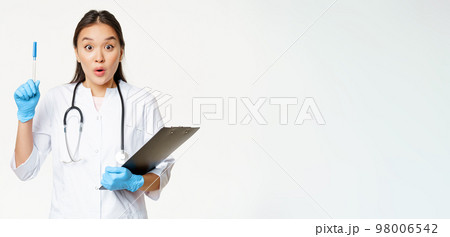 Enthusiastic nurse, asian woman doctor raising pen up, holding clipboard with patient papers, standing in uniform over white background Enthusiastic nurse, asian woman doctor raising pen up, holding clipboard with patient papers, standing in uniform over white background 98006542