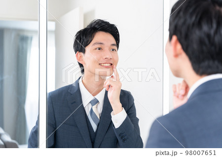 鏡を見て歯のチェックをするビジネスマン（ホワイトニング・歯並び・歯列矯正） 98007651