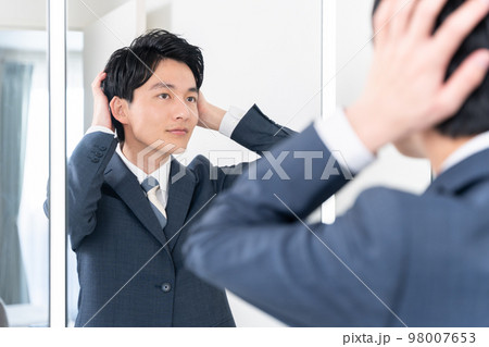 洗面所で鏡を見てヘアセットする若いビジネスマン（髪の毛・朝・出勤準備） 98007653