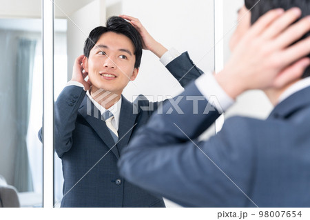 洗面所で鏡を見てヘアセットする若いビジネスマン（髪の毛・朝・出勤準備） 98007654