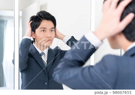洗面所で鏡を見てヘアセットする若いビジネスマン（髪の毛・朝・出勤準備） 98007655