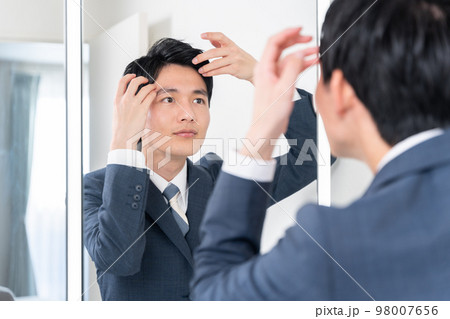 洗面所で鏡を見てヘアセットする若いビジネスマン（髪の毛・朝・出勤準備） 98007656