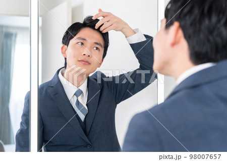 洗面所で鏡を見てヘアセットする若いビジネスマン（髪の毛・朝・出勤準備） 98007657