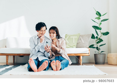 リビングでスマホを見る若い夫婦 98007683