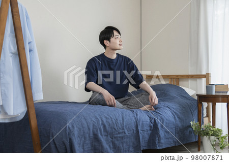 ベッドの上に座った若い男性 98007871