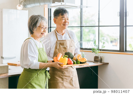 家のキッチンの前で笑顔で話すアジア人高齢者夫婦（料理教室） 98011407