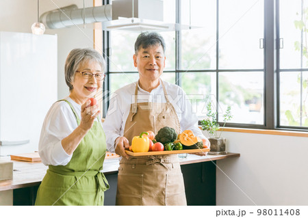 家のキッチンの前で笑顔で話すアジア人高齢者夫婦（料理教室） 98011408
