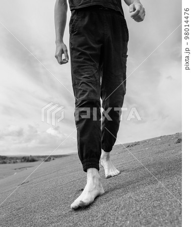 Young man walking alone on the sand in sandy desert Young man walking alone on the sand in sandy desert 98014476