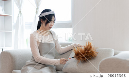 Housewife holding a dusting brush to clean things Pillows, rugs and other things in the living room, Big cleaning, Daily routine ,Removes germs and dirt and deep stains, Spray alcohol. 98015368