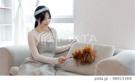 Housewife holding a dusting brush to clean things Pillows, rugs and other things in the living room, Big cleaning, Daily routine ,Removes germs and dirt and deep stains, Spray alcohol. 98015369