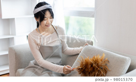 Housewife holding a dusting brush to clean things Pillows, rugs and other things in the living room, Big cleaning, Daily routine ,Removes germs and dirt and deep stains, Spray alcohol. 98015370