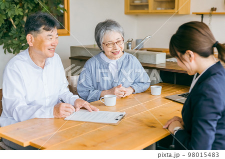 契約書にサインをするアジア人高齢者夫婦とスーツ姿のビジネスウーマン 98015483